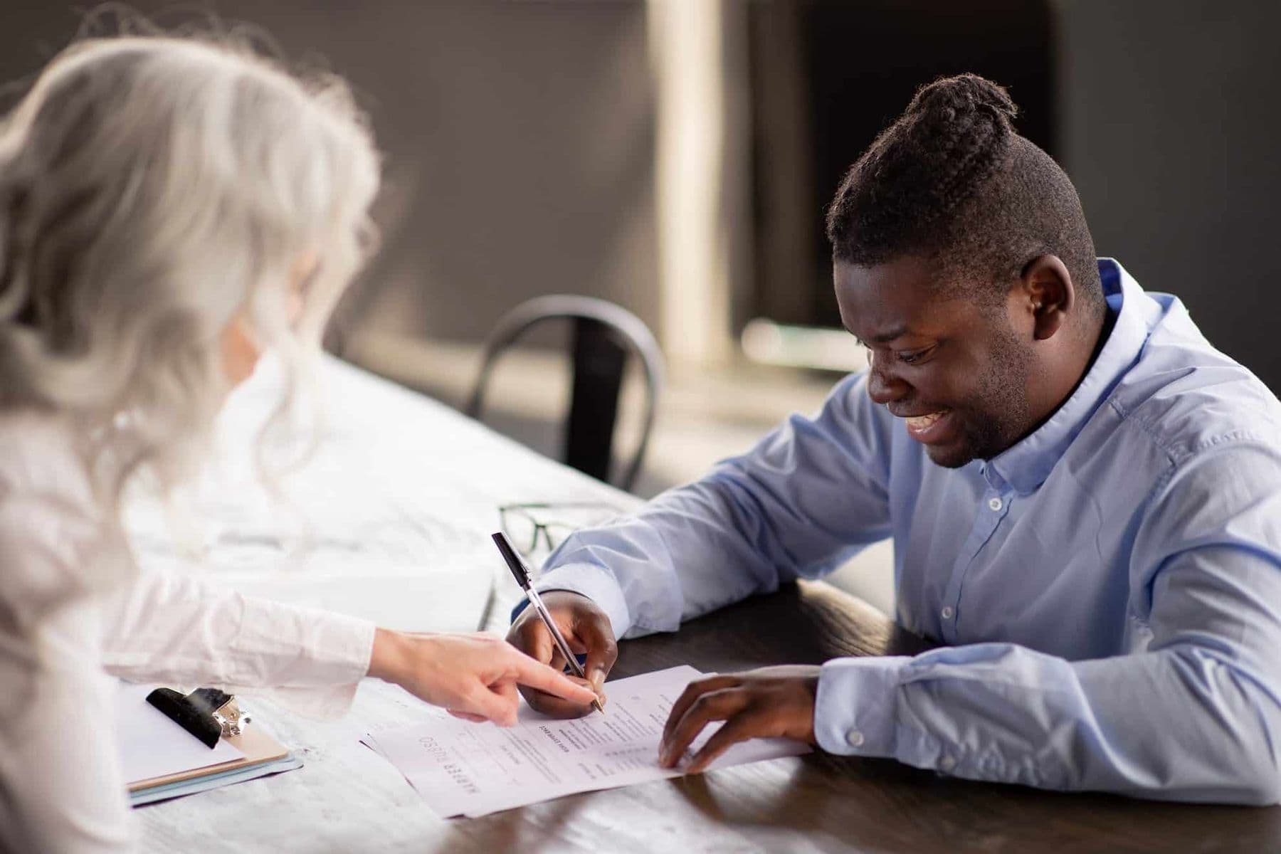 Smiling man signing power of attorney documents with professional assistance at a legal or notary office in Dubai.