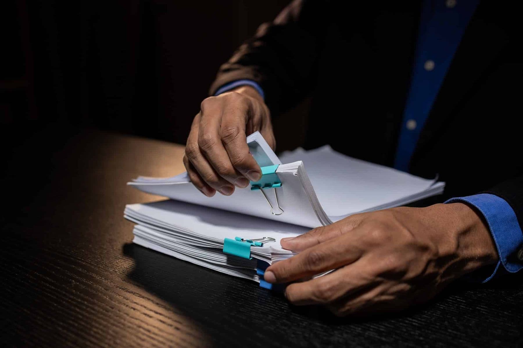 Person organizing corporate tax registration documents with binder clips on a desk.
