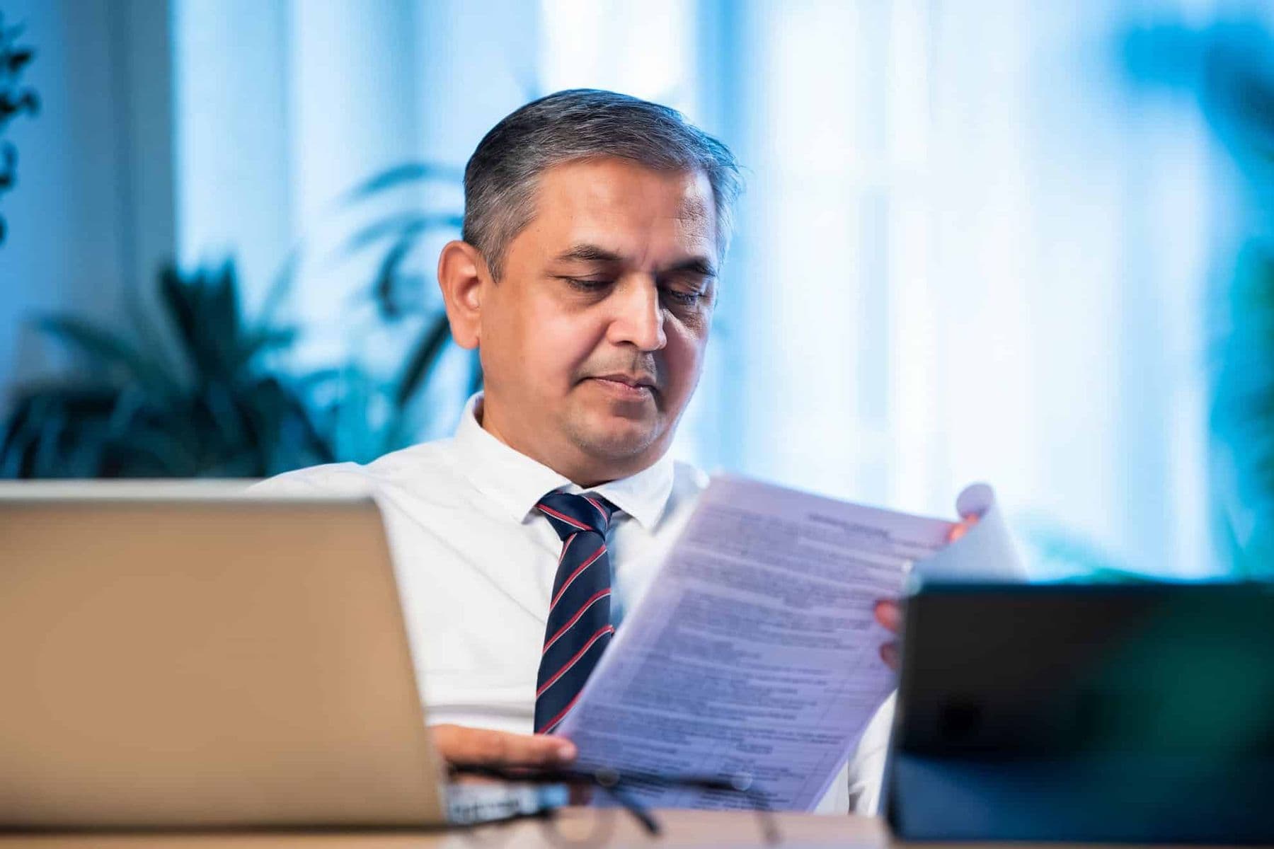 Middle-aged businessman in formal attire reviewing tax documents at a desk with a laptop, representing VAT compliance and reverse charge mechanism in the UAE.
